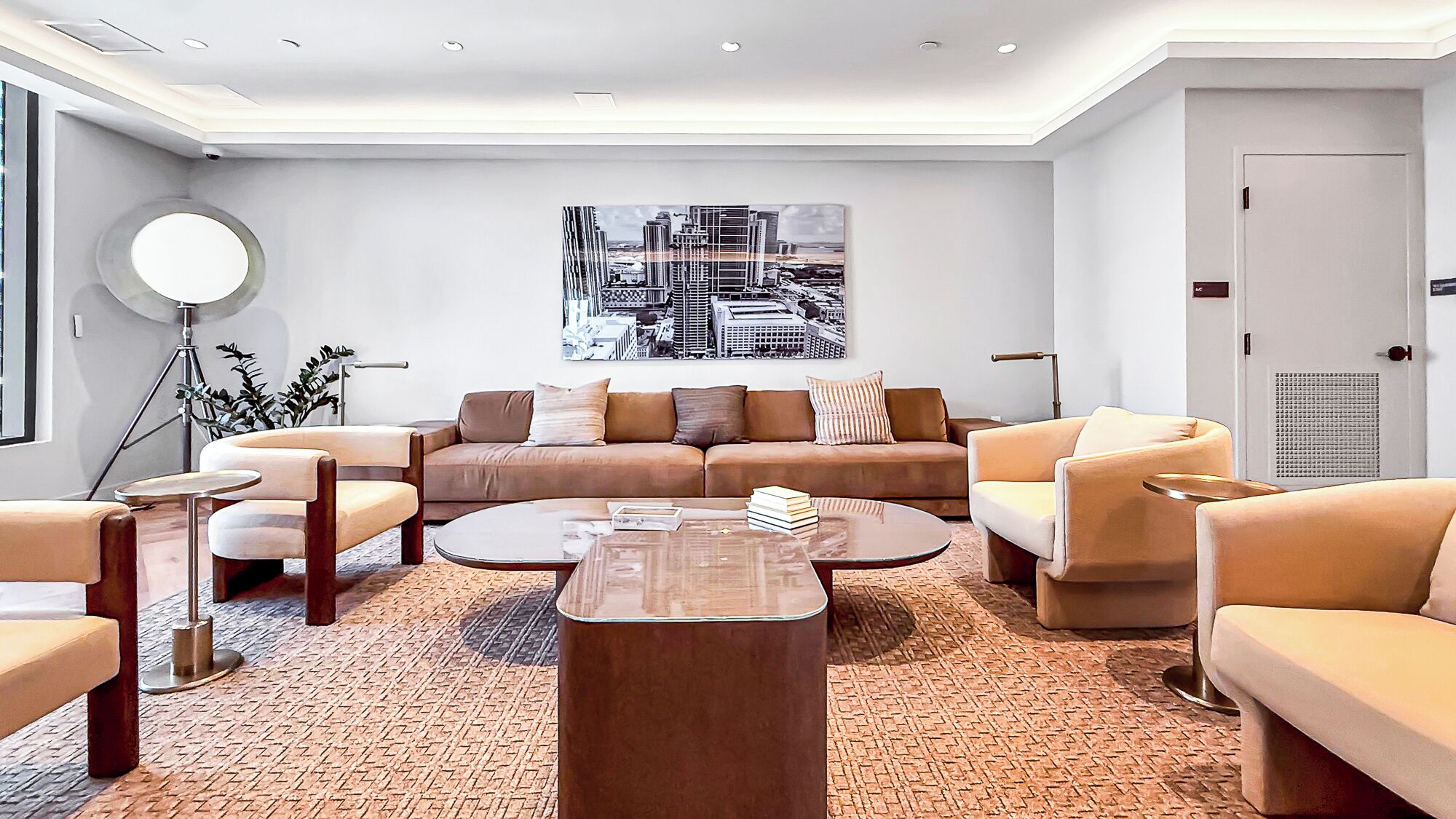 A modern living room with a sofa, armchairs, a coffee table, and a cityscape painting on the wall.