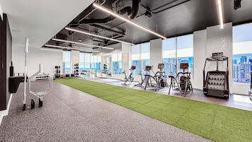 Un gimnasio con equipo de ejercicio, una zona de césped artificial y amplios ventanales con vistas a la ciudad.