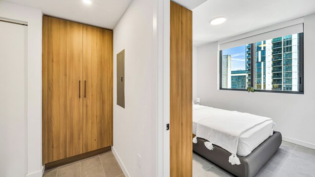 A bedroom with a bed, a window with a city view, a wooden wardrobe, and a door. - Miami Central Suites (Miami)