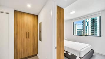 Un dormitorio con una cama, un ventanal con vista a la ciudad, un armario de madera y una puerta.
