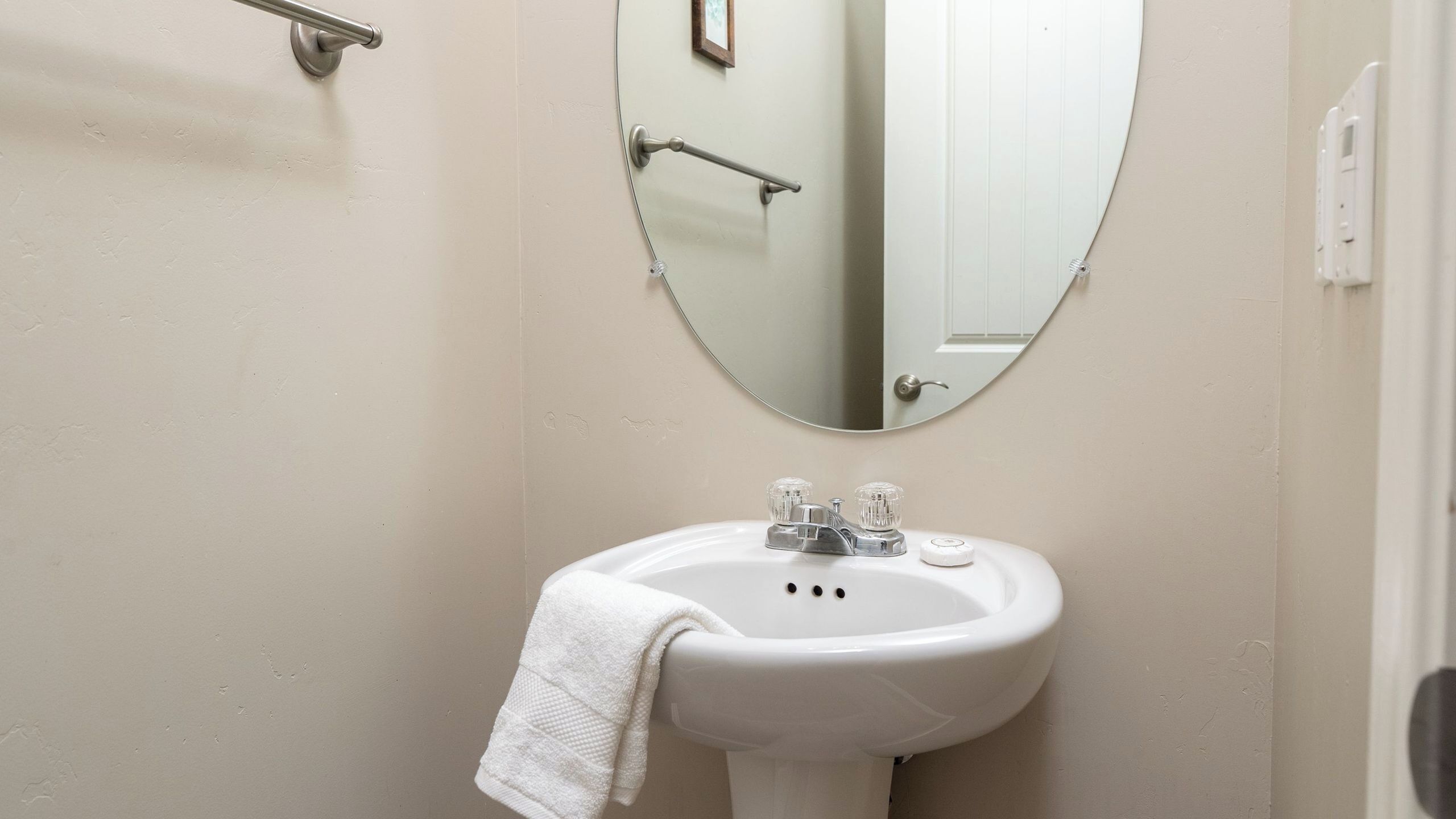 A bathroom with a white sink, a round mirror, and a towel hanging on the sink.