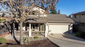 Ein Wohnhaus mit Garage, überdachter Veranda und einem Baum mit kargen Blättern.