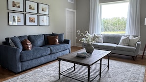 A living room with two sofas, a coffee table, and framed pictures on the wall. - Experience Autumn Hill - A 7 Bedroom Farmhouse on Two Lakes in Clermont, FL (Clermont)