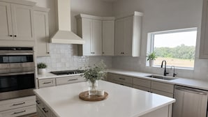 Una cucina moderna con mobili bianchi, un'isola centrale, forno integrato e una finestra con vista sul verde.