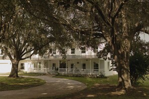 A two-story building with a covered porch, large trees, and a paved driveway.
