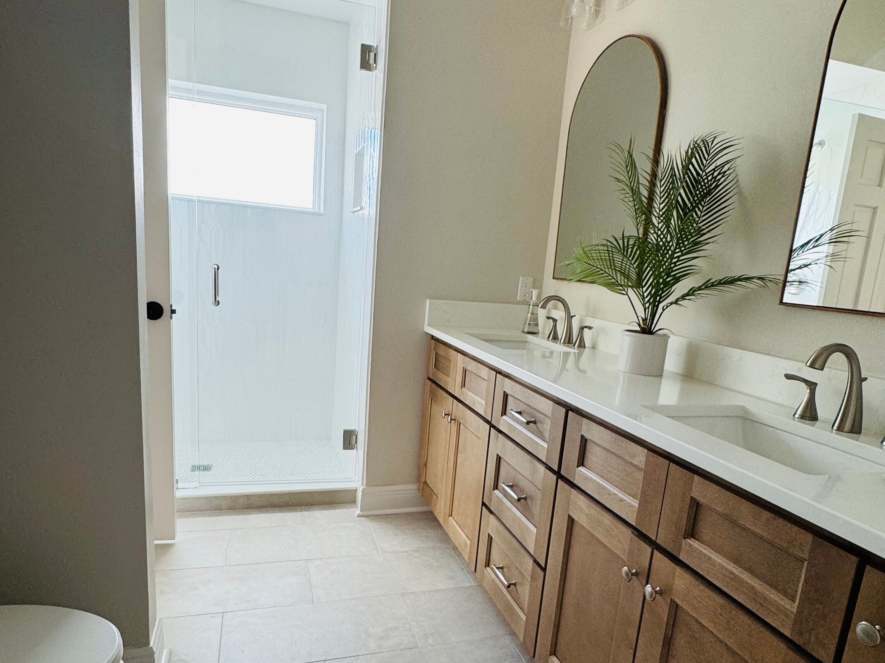 A bathroom with a white door, a sink with a mirror, and a potted plant.
