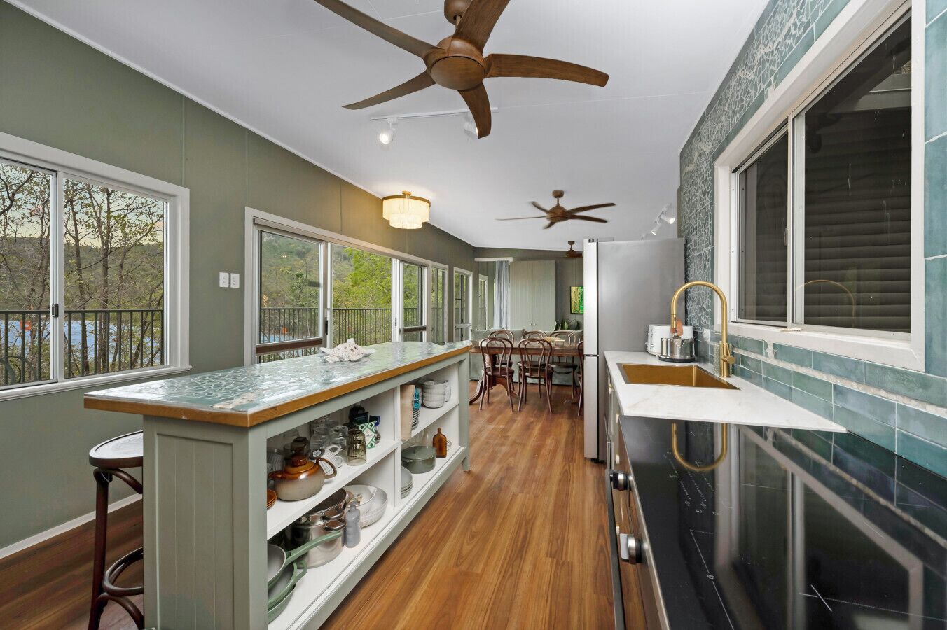 A modern kitchen with a central island, wooden flooring, and a view of the outdoors.