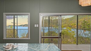 A room with a glass-top table, a view of a lake through large windows, and a balcony with a railing. - AMAROO ARCADIA – GABUL WAY (Arcadia)
