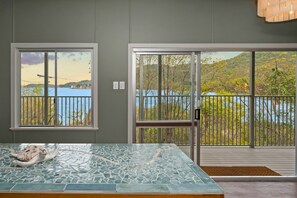 A room with a glass-top table, a view of a lake through large windows, and a balcony with a railing. - AMAROO ARCADIA – GABUL WAY (Arcadia)