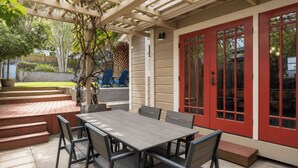 An outdoor patio with a wooden table and chairs, a red door, and a pergola structure. - Backyard Vines on Olive by Avantstay Spa + BBQ + Big Backyard Walk to Downtown Paso (Paso Robles)