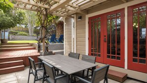 An outdoor patio with a wooden table and chairs, a red door, and a pergola structure. - Backyard Vines on Olive by Avantstay Spa + BBQ + Big Backyard Walk to Downtown Paso (Paso Robles)