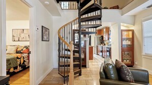 A spacious living area with a spiral staircase, a sofa set, and a kitchen in the background. - Backyard Vines on Olive by Avantstay Spa + BBQ + Big Backyard Walk to Downtown Paso (Paso Robles)