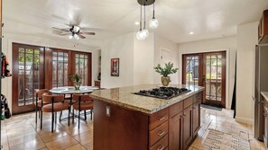 A kitchen with a central island, a ceiling fan, pendant lights, and a dining area with chairs. - Backyard Vines on Olive by Avantstay Spa + BBQ + Big Backyard Walk to Downtown Paso (Paso Robles)