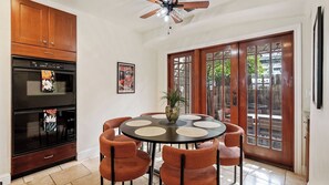 A dining area with a round table, six chairs, a ceiling fan, and a kitchen with an oven and cabinets. - Backyard Vines on Olive by Avantstay Spa + BBQ + Big Backyard Walk to Downtown Paso (Paso Robles)