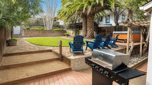 Un patio trasero con una parrilla, sillas azules y un sendero de piedra.
