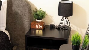 A bedside table with a digital clock, a lamp, and a small plant. - Backyard Vines on Olive by Avantstay Spa + BBQ + Big Backyard Walk to Downtown Paso (Paso Robles)