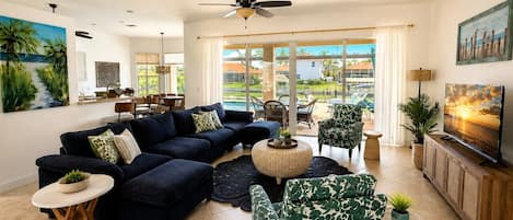 A spacious living room with a dark blue sectional sofa, a round coffee table, and a television on a wooden cabinet.