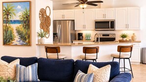 A modern kitchen with white cabinets, stainless steel appliances, and a dining area with a blue sofa and chairs. - Gullaby Getaway - Pool, Wide Canal, Sleeps 7 (Cape Coral)
