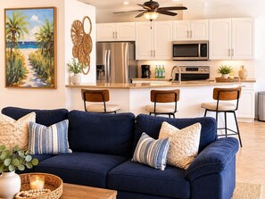 A modern kitchen with white cabinets, stainless steel appliances, and a dining area with a blue sofa and chairs. - Gullaby Getaway - Pool, Wide Canal, Sleeps 7 (Cape Coral)