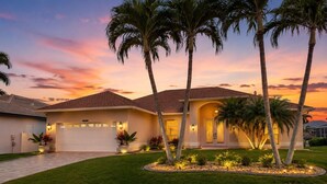 A residential house with a garage, palm trees, and a well-maintained lawn. - Gullaby Getaway - Pool, Wide Canal, Sleeps 7 (Cape Coral)