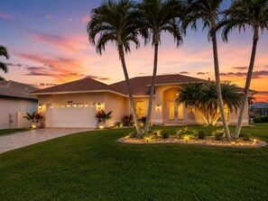 A residential house with a garage, palm trees, and a well-maintained lawn. - Gullaby Getaway - Pool, Wide Canal, Sleeps 7 (Cape Coral)