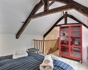 Ein Schlafzimmer mit schrägem Dach, einem Bett mit gestreifter Bettwäsche, einem roten Kleiderschrank und einem kleinen Tisch.