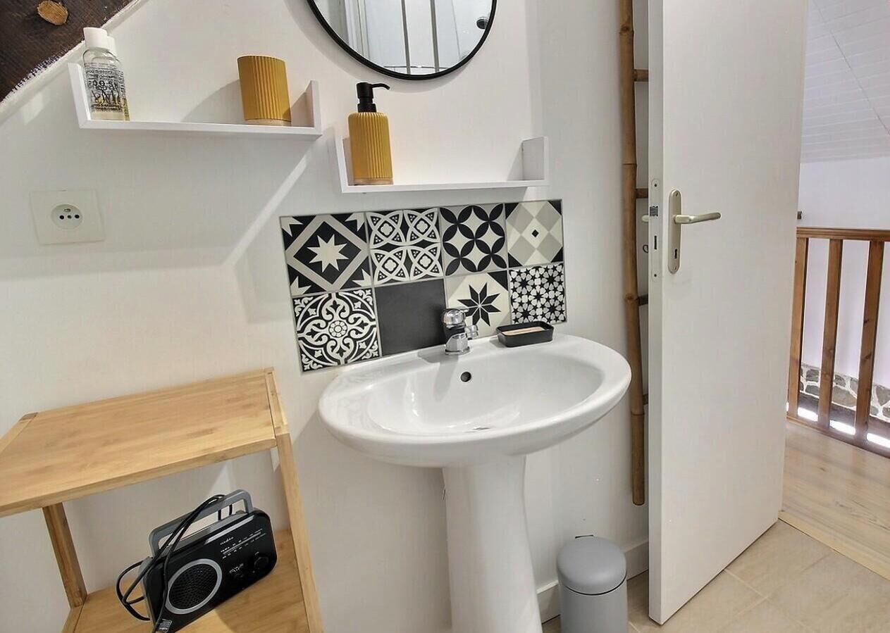 A bathroom with a white sink, a mirror, a toilet, and a wooden shelf with a radio.