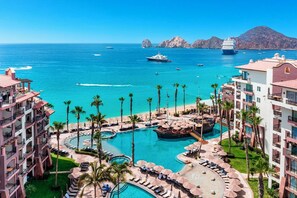 A resort with multiple swimming pools, palm trees, and a view of the ocean with boats. - Luxury Pool-View Studio at 5-Star Villa del Arco– Steps to Medano Beach! (cabo san lucas)