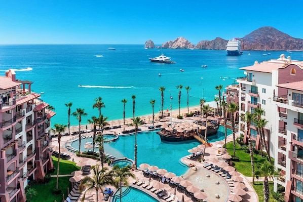 Un complex turístic amb diverses piscines, palmeres i vista a l'oceà amb vaixells.