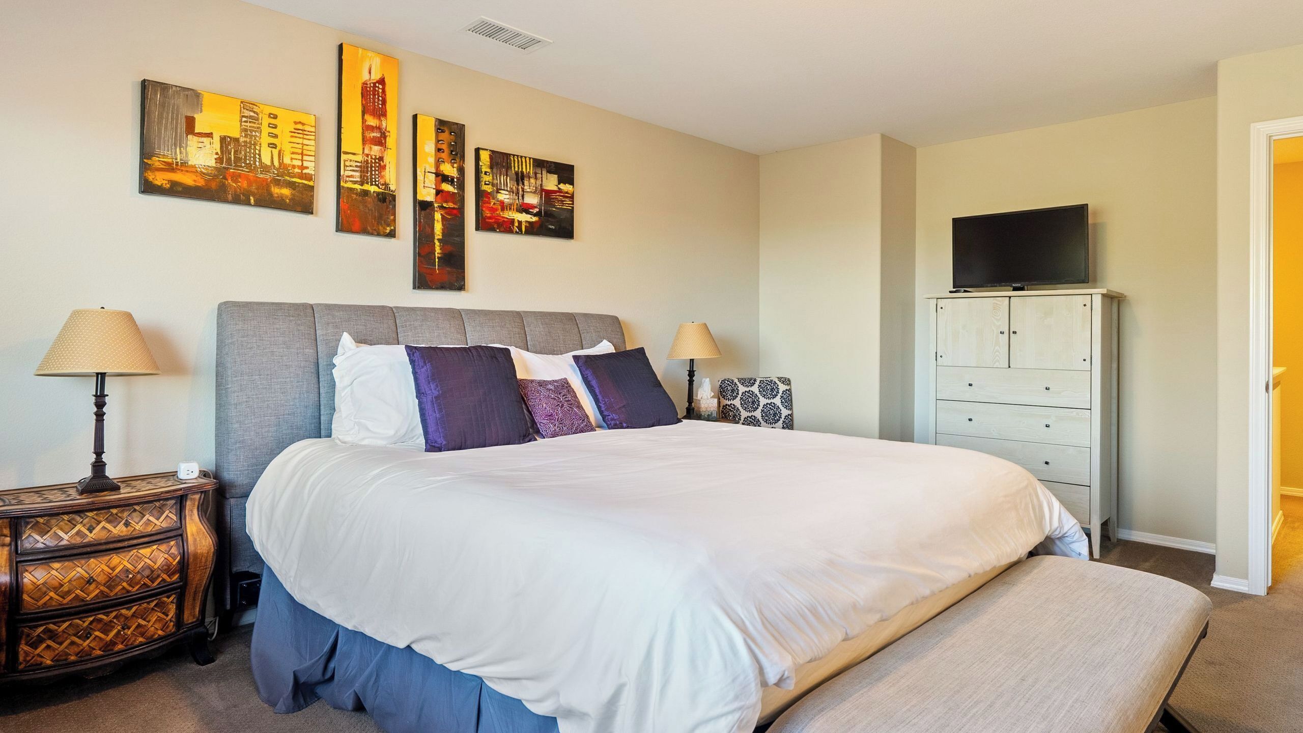 A hotel room with a large bed, two bedside tables, a TV on a cabinet, and artwork on the wall.