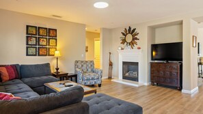 A living room with a sofa, armchair, fireplace, television, and decorative wall art. - Sunset Summit by Avantstay Modern Kitchen + BBQ Patio Downtown Paso Robles (Paso Robles)
