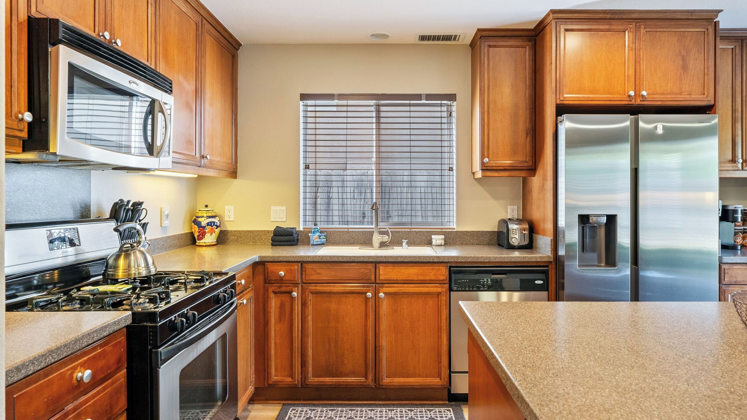 A modern kitchen with wooden cabinets, stainless steel appliances, and a granite countertop.