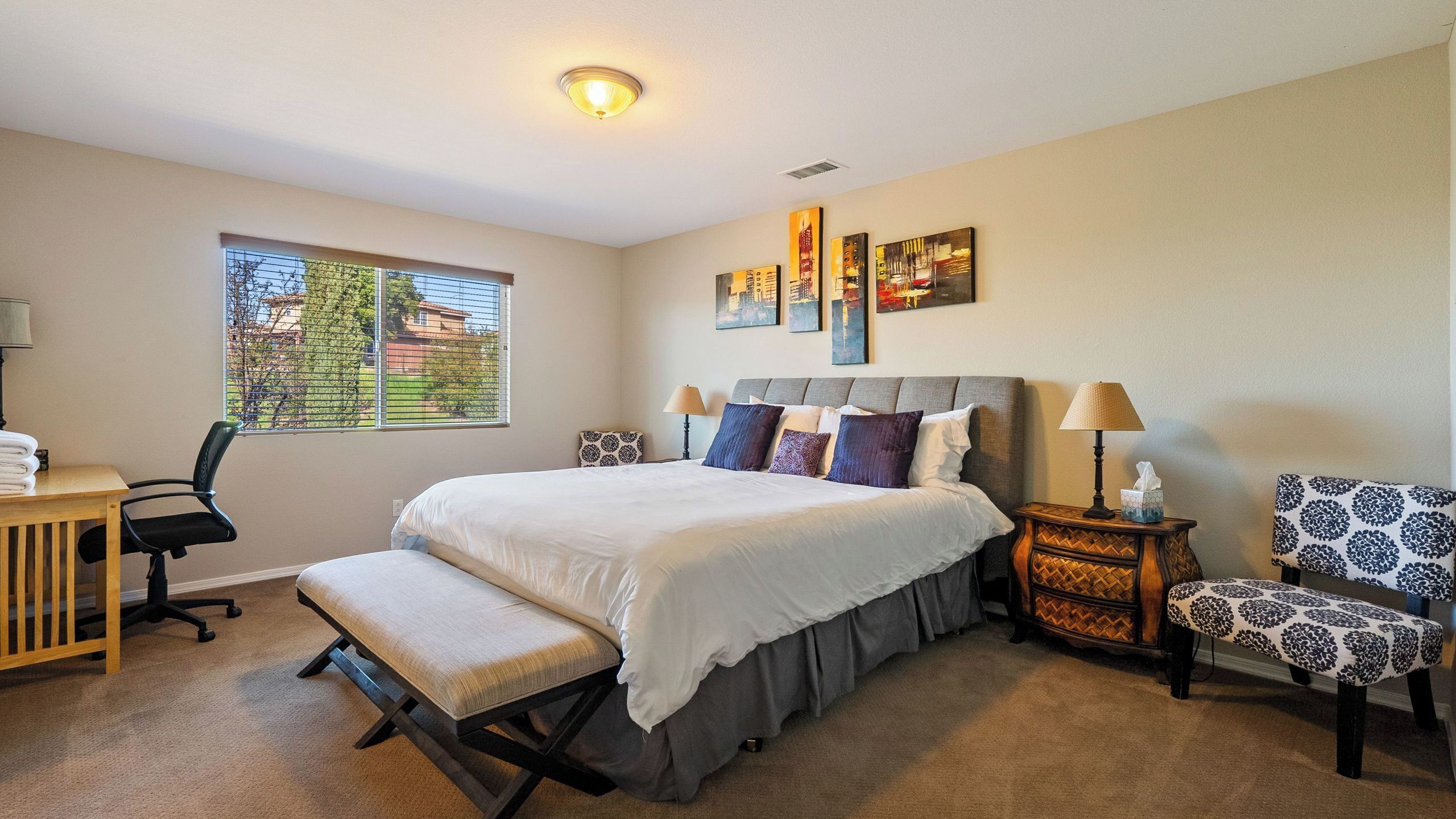 A hotel room with a large bed, a desk, a chair, and a window with a view of the outside.
