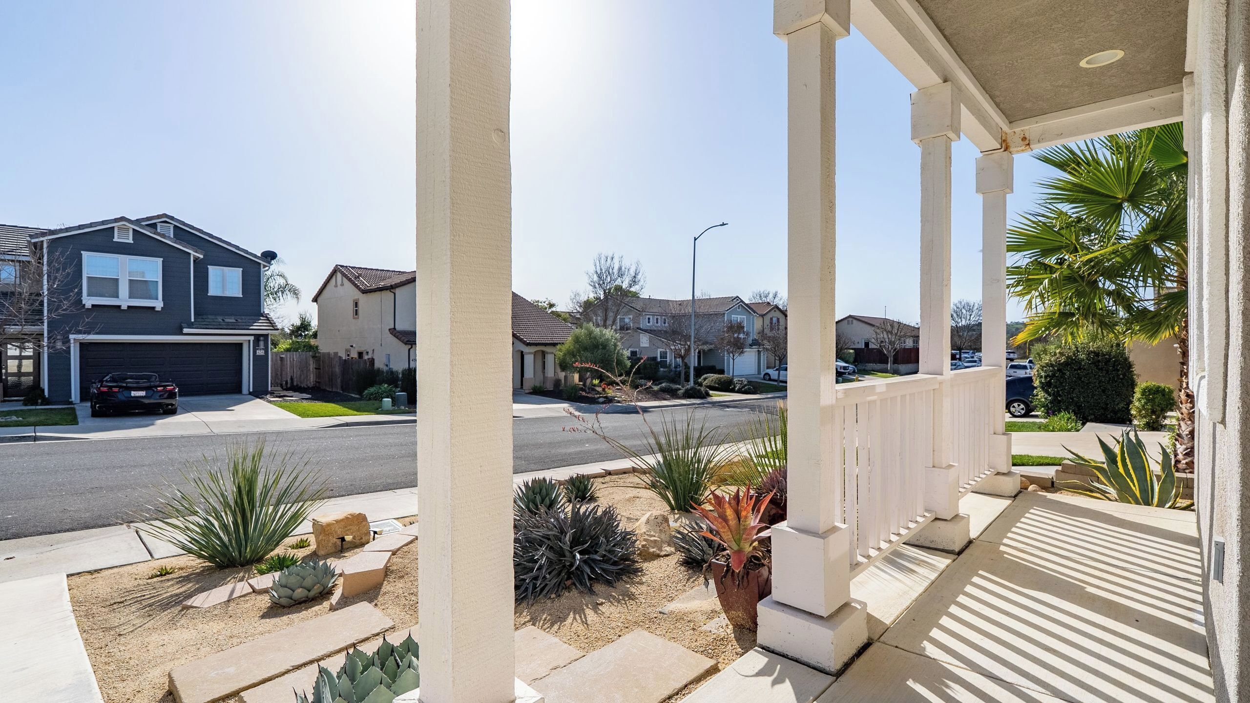 A residential street with houses, a covered porch, and landscaping.