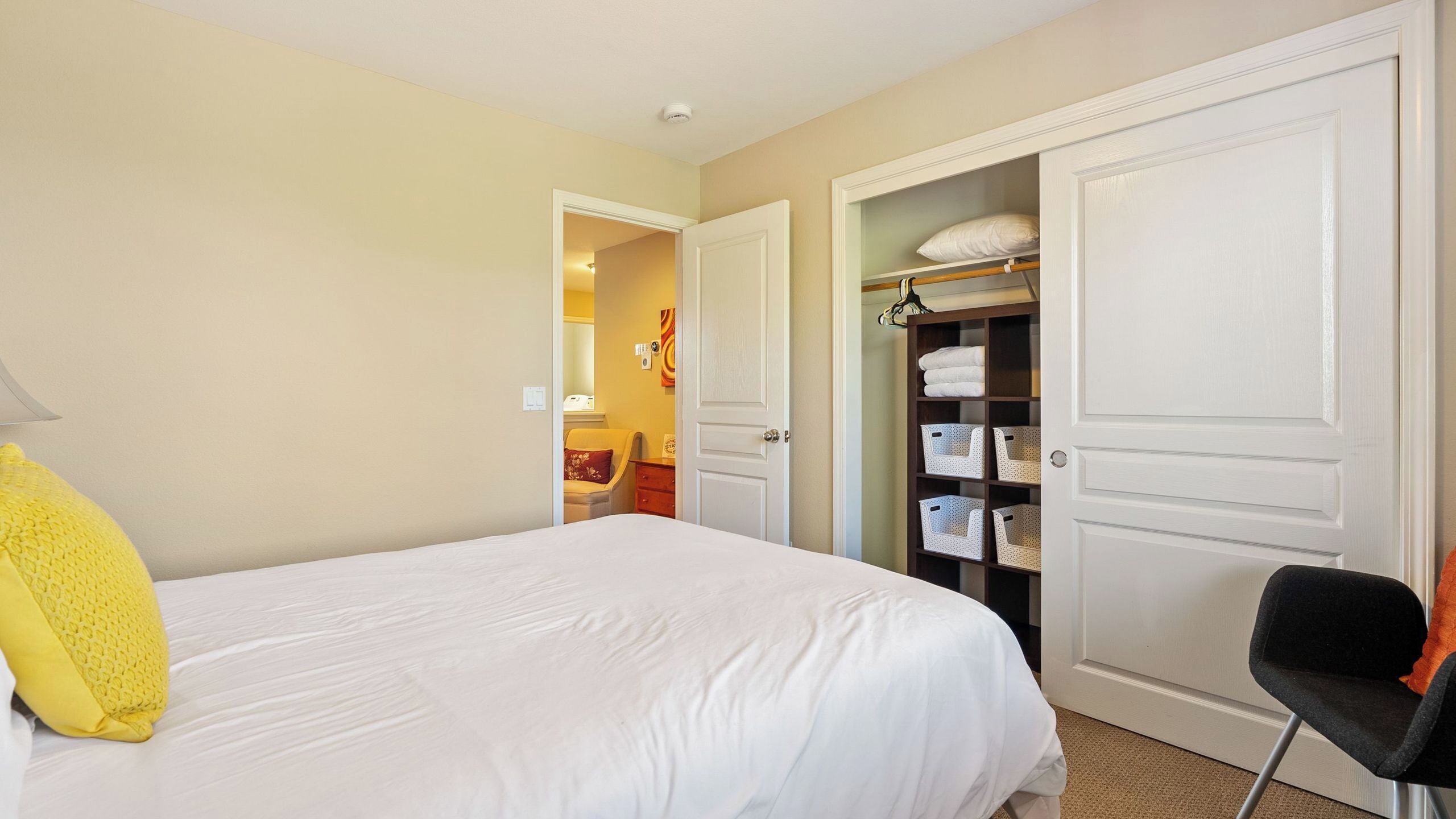 A hotel room with a bed, a chair, a wardrobe, and a closet with shelves.