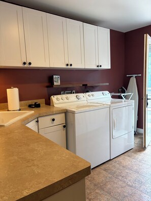 A laundry area with a washing machine and dryer, a towel dispenser, and a small shelf with a book. - Gorgeous 4-bedroom house in charming Dodgeville. (Dodgeville)