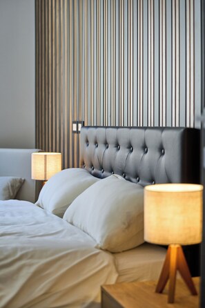 A neatly made bed with a tufted headboard, two bedside lamps, and a striped wall in the background.