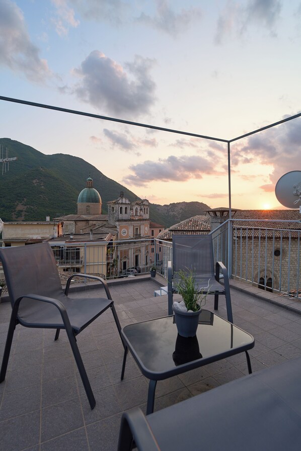 A terrace with two chairs and a table, overlooking a historic building with a dome and bell tower, under a clear sky.