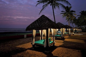 Una playa con cabañas de techo de paja y sillones de jardín verdes.