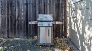 A Weber Spirit portable grill with two control knobs, positioned outdoors with a wooden fence and a house in the background. - Quercus Acorn Cottage by Avantstay 2 King Suites + Porch Walkable Downtown Paso Robles (Paso Robles)