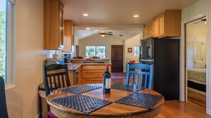 A kitchen with wooden cabinets, a dining table with black placemats, and a ceiling fan. - Quercus Acorn Cottage by Avantstay 2 King Suites + Porch Walkable Downtown Paso Robles (Paso Robles)
