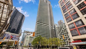 A tall, modern skyscraper with a grid-like facade, surrounded by other high-rise buildings and a clear blue sky.