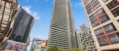 A tall, modern skyscraper with a grid-like facade, surrounded by other high-rise buildings and a clear blue sky.