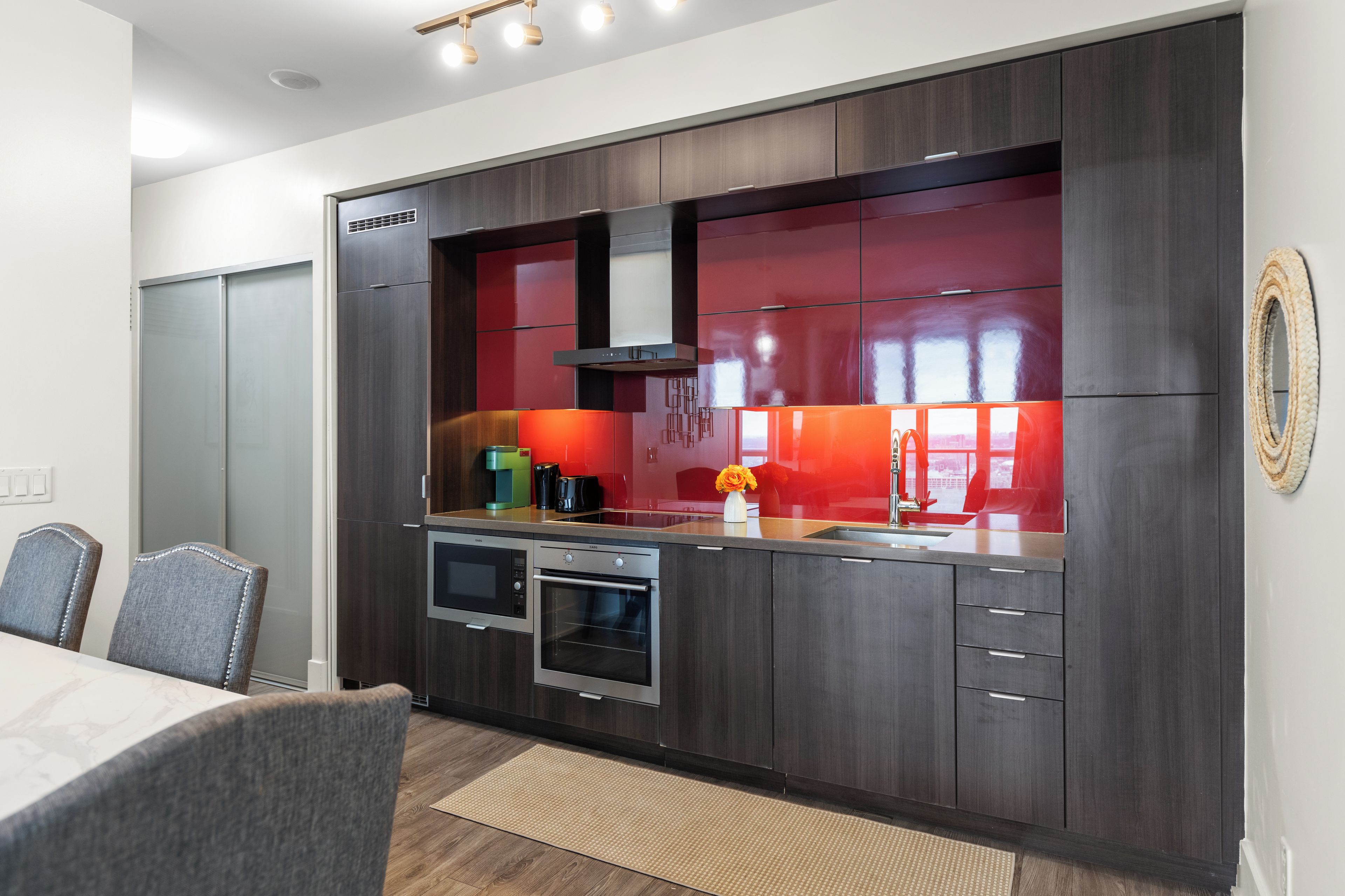 Una cocina moderna con gabinetes de madera oscura, electrodomésticos de acero inoxidable y un salpicadero rojo.