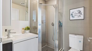 Un baño moderno con cabina de ducha de vidrio, un lavamanos blanco y un inodoro.