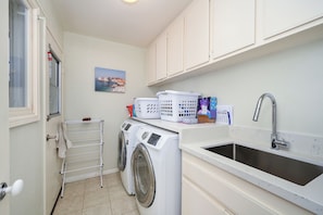 A laundry room with a washing machine, a drying rack, a sink, and a window with a view of a coastal town. - Modern Home in a Quiet-Gated area w/ Pool & Spa. (Corona Del Mar)