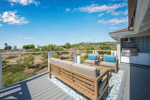 A deck with a sofa and chairs, a barbecue grill, and a view of a hilly landscape. - Modern Home in a Quiet-Gated area w/ Pool & Spa. (Corona Del Mar)