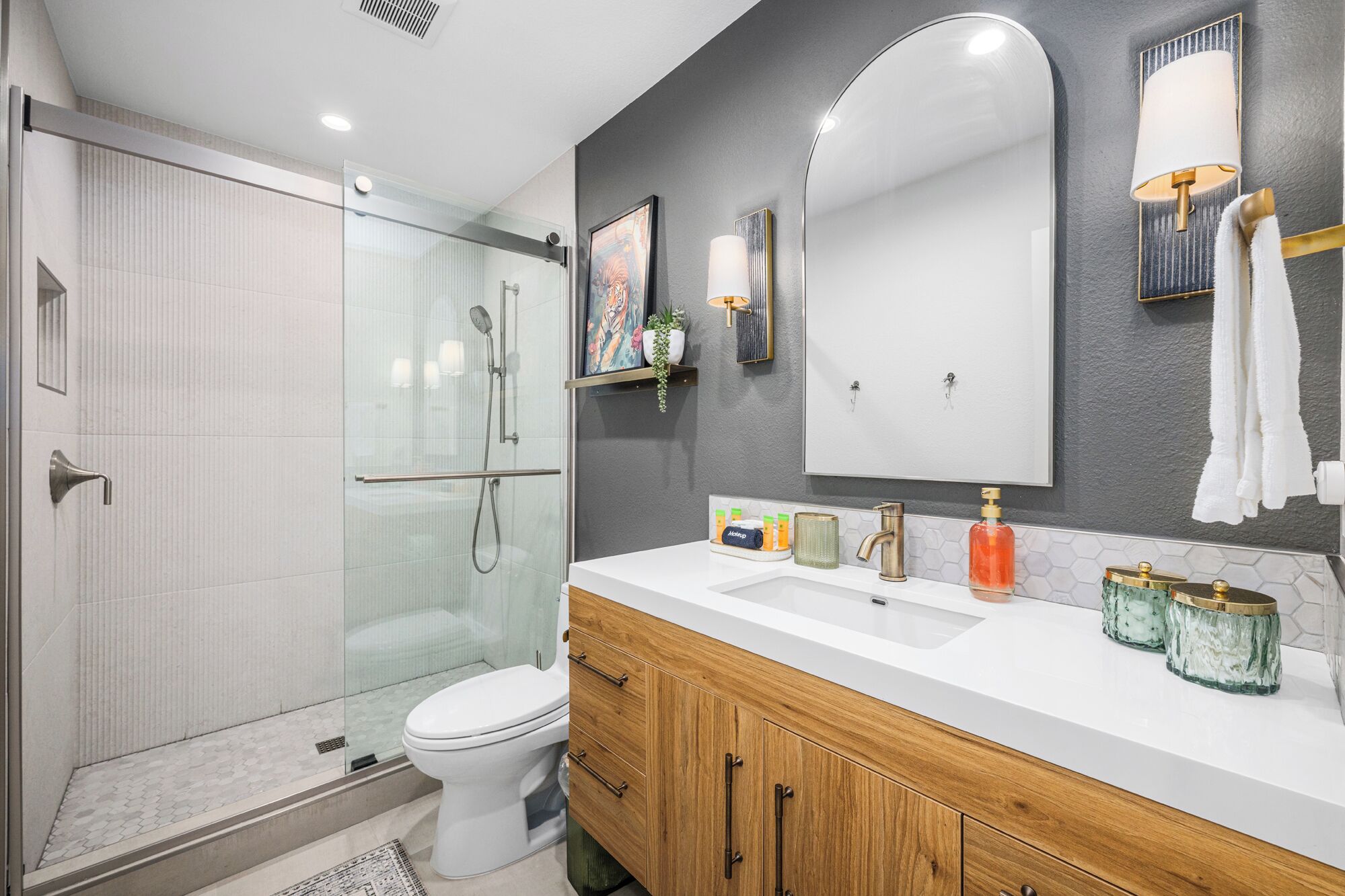 A modern bathroom with a glass shower enclosure, a white toilet, a vanity with a mirror, and a sink.
