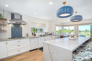 A modern kitchen with a central island, white cabinetry, and a large window providing a view of the outdoors. - Modern Home in a Quiet-Gated area w/ Pool & Spa. (Corona Del Mar)