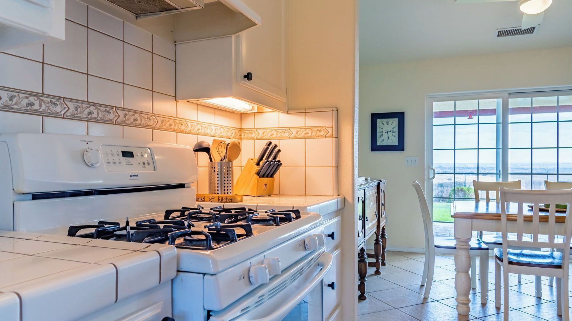 A modern kitchen with a gas stove, oven, and a view of the outdoors through a large window.